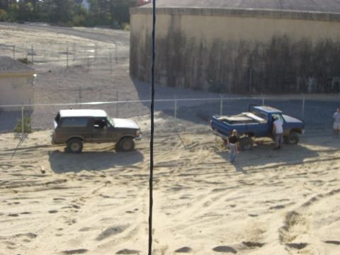 1994 Ford Bronco - Two trucks are parked on a sandy lot next to a large cylindrical building.