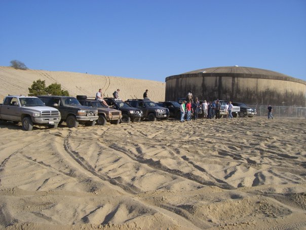 Group of SUVs and trucks on sand dunes with a large concrete structure