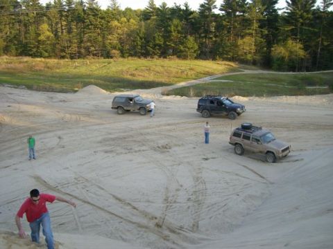 1994 Ford Bronco - Several off-road vehicles are parked in a sandy area with people nearby.