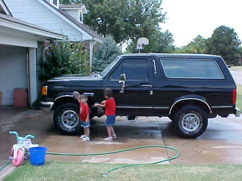 1989 Ford Bronco - Children washing a black Ford Bronco in the driveway on a sunny day.