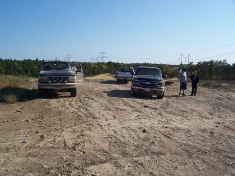 1994 Ford Bronco - A 1994 Ford Bronco is seen from the front on a dirt road, accompanied by two other trucks under a clear blue sky.