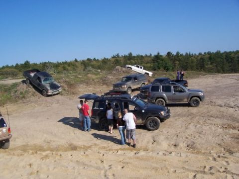 1994 Ford Bronco - Several SUVs and trucks are parked on a dirt terrain under a clear blue sky.
