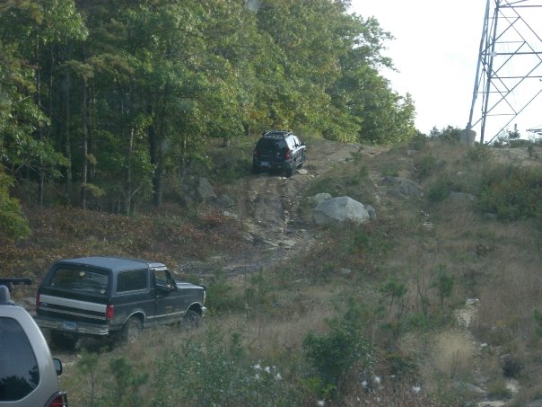 Black Ford Bronco with silver trim driving on a dirt hill, rear quarter view