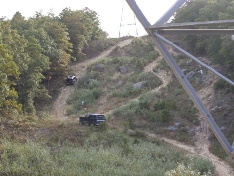 1994 Ford Bronco - Two Ford Broncos navigate a winding dirt path up a wooded hillside.