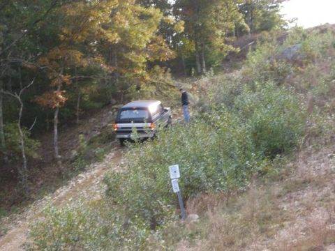 1994 Ford Bronco - A Ford Bronco navigates a wooded trail on an incline, with a person observing.