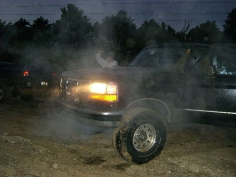1994 Ford Bronco - A black 1994 Ford Bronco is seen from the front-three-quarter view, emitting smoke with its headlights illuminated.