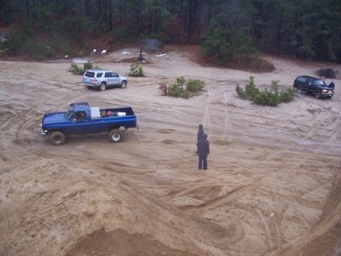 1994 Ford Bronco - Multiple vehicles navigate a sandy off-road terrain with trees and overcast skies.