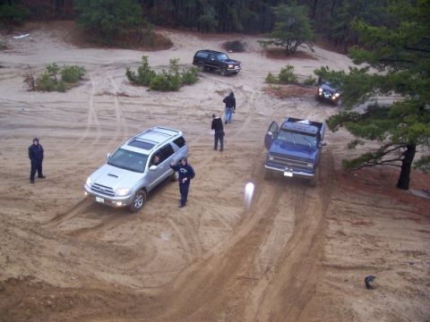 1994 Ford Bronco - Multiple vehicles navigate a sandy off-road course with trees and dirt mounds visible in the background.