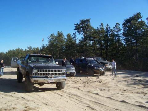 1994 Ford Bronco - Several off-road vehicles are gathered on a sandy terrain under a clear blue sky.