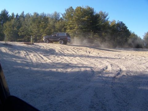 1994 Ford Bronco - Ford Bronco driving on a dirt road, kicking up dust under a clear blue sky.