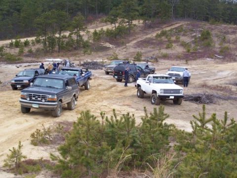 1994 Ford Bronco - A group of off-road vehicles are gathered in a sandy, wooded area.