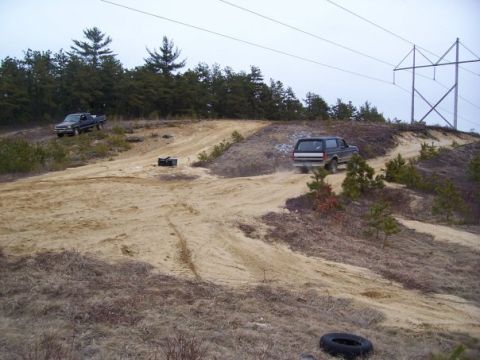 1994 Ford Bronco - A dark SUV navigates a sandy track on a hill, with another truck visible in the background.