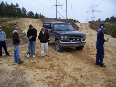 1994 Ford Bronco - A group of friends stand around a dark blue Ford Bronco in a sandy, off-road area with power lines overhead.