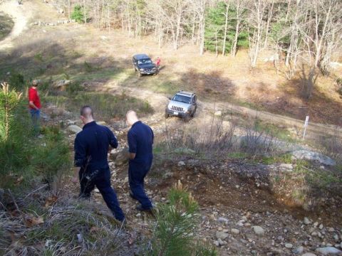 1994 Ford Bronco - Two SUVs navigate a dirt road in a wooded, hilly terrain with several people present.