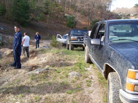 1994 Ford Bronco - Several trucks and people are gathered on a dirt road in a wooded area.