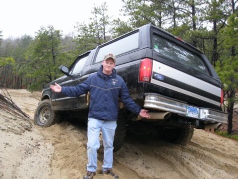 1994 Ford Bronco - A man poses with a black Ford Bronco stuck on a sandy hill, showing off the rear of the vehicle.