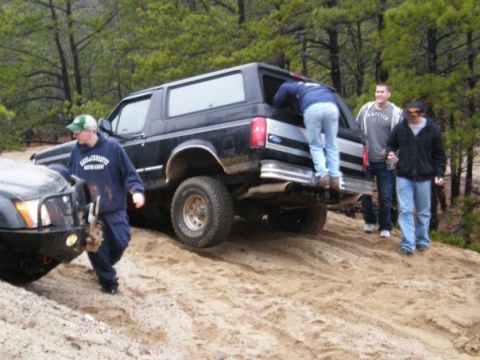 1994 Ford Bronco - A group of friends are gathered around a black 1994 Ford Bronco on a sandy off-road trail.