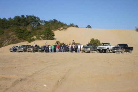 1994 Ford Bronco - Several off-road vehicles and a group of people gathered on a sandy landscape under a clear blue sky.