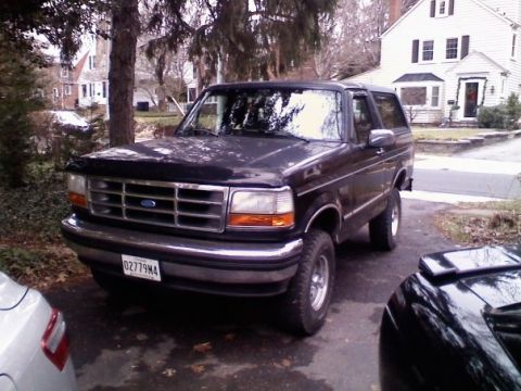 1994 Ford Bronco - A dark-colored Ford Bronco is parked in a driveway with a house and trees in the background.