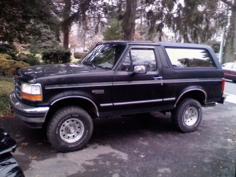 1994 Ford Bronco - This black 1994 Ford Bronco SUV is seen from the side, parked outdoors with trees and a house visible.