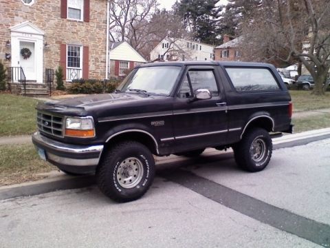 1994 Ford Bronco - This black Ford Bronco is parked on a residential street in front of a stone house.