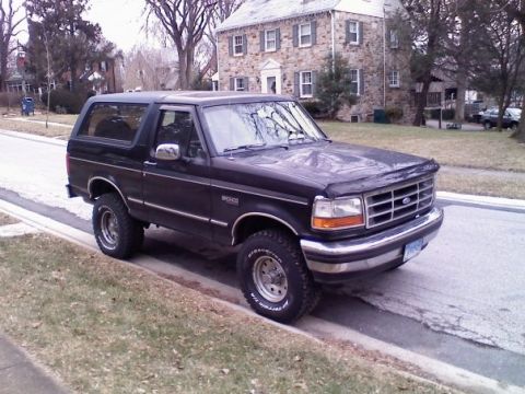 1994 Ford Bronco - A black Ford Bronco is parked on the side of a street in front of a stone house.