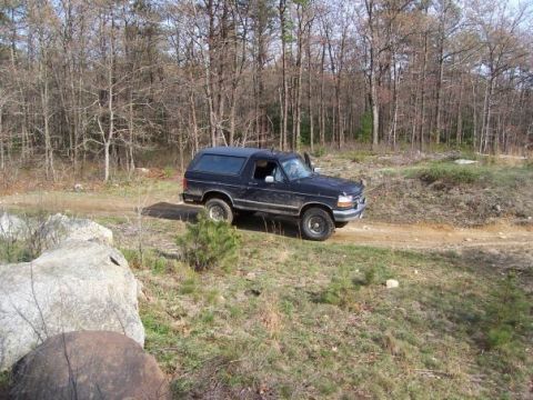 1994 Ford Bronco - A black 1994 Ford Bronco navigates a dirt path through a wooded landscape.