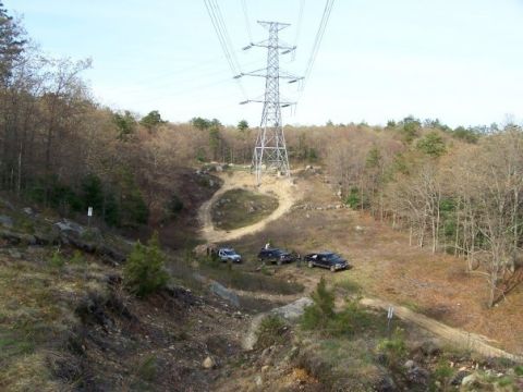 1994 Ford Bronco - Several SUVs are parked on a dirt trail in a wooded area with a large power line tower overhead.