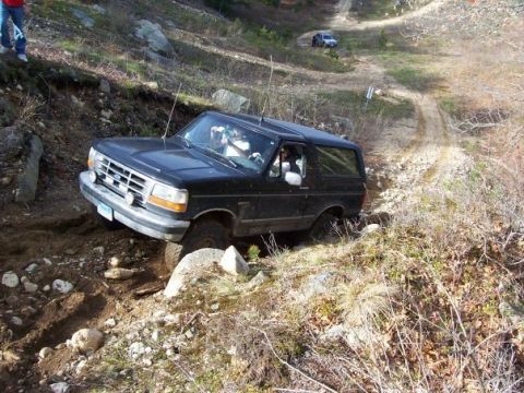 1994 Ford Bronco - A black Ford Bronco tackles a challenging off-road path with another vehicle visible in the distance.