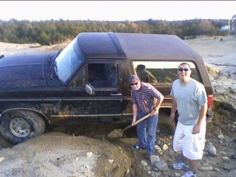 1994 Ford Bronco - A black Ford Bronco is stuck in the dirt with two men standing next to it.