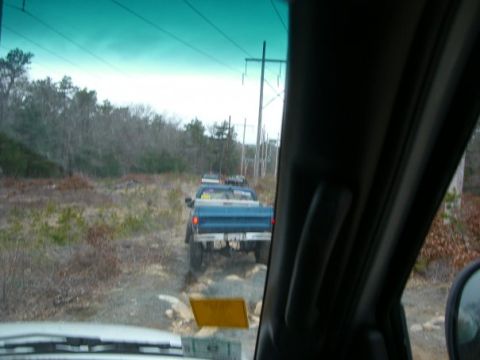 1994 Ford Bronco - A convoy of trucks navigates a rough dirt path through a wooded area.