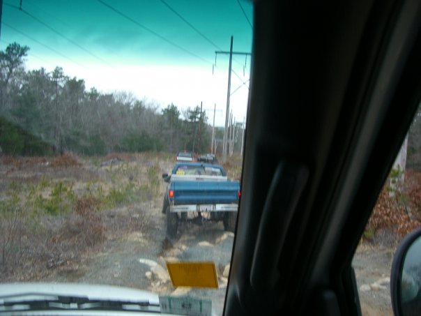 Driving behind a blue pickup truck on a dirt road with trees and power lines