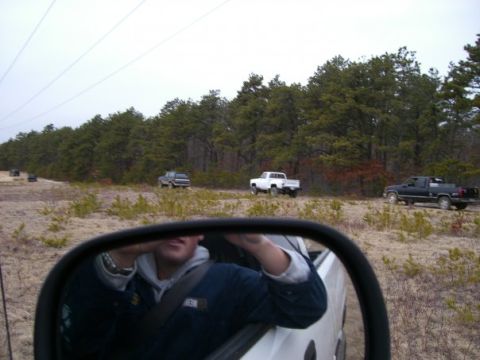 1994 Ford Bronco - Several trucks are seen on a dirt road surrounded by trees, viewed from a side mirror.
