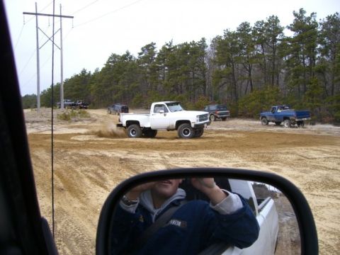 1994 Ford Bronco - Several trucks and SUVs are seen off-roading on a dirt path surrounded by trees.