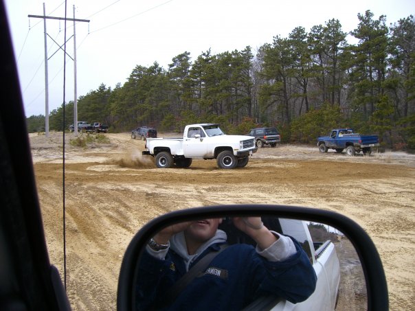 White pickup truck kicking up dust on a dirt road with other trucks and SUVs in the background