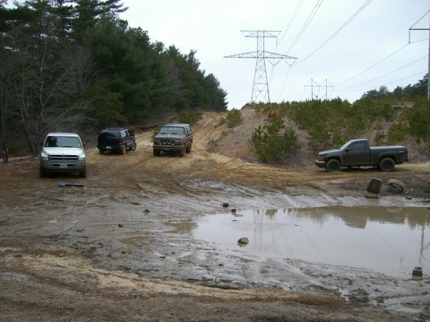 Four-wheel drive vehicles on a muddy trail with power lines overhead