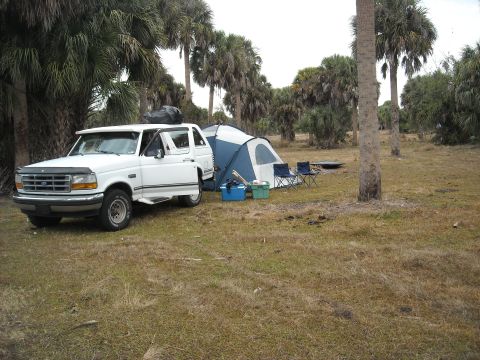 1992 Ford Bronco - A white 1992 Ford Bronco is parked at a campsite with a tent and chairs nearby.