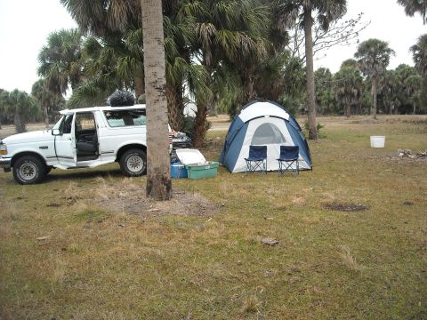 1992 Ford Bronco - A white 1992 Ford Bronco is parked at a campsite next to a blue and white tent, with camping gear nearby.