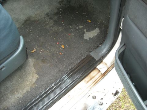 1992 Ford Bronco - The interior floor of a vehicle shows dirt, water, and debris, indicating a need for cleaning.