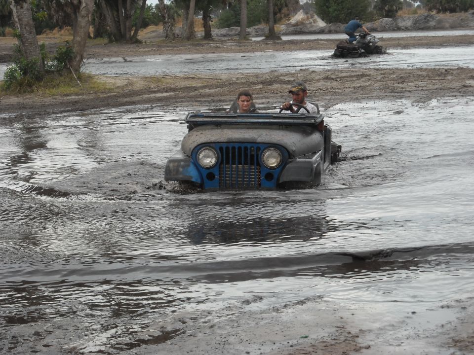 Blue Jeep driving through mud with two people inside