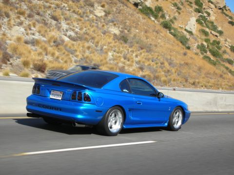 1998 Ford Crown Victoria - Blue 1998 Ford Mustang Cobra seen on the highway, with another vehicle in the background.