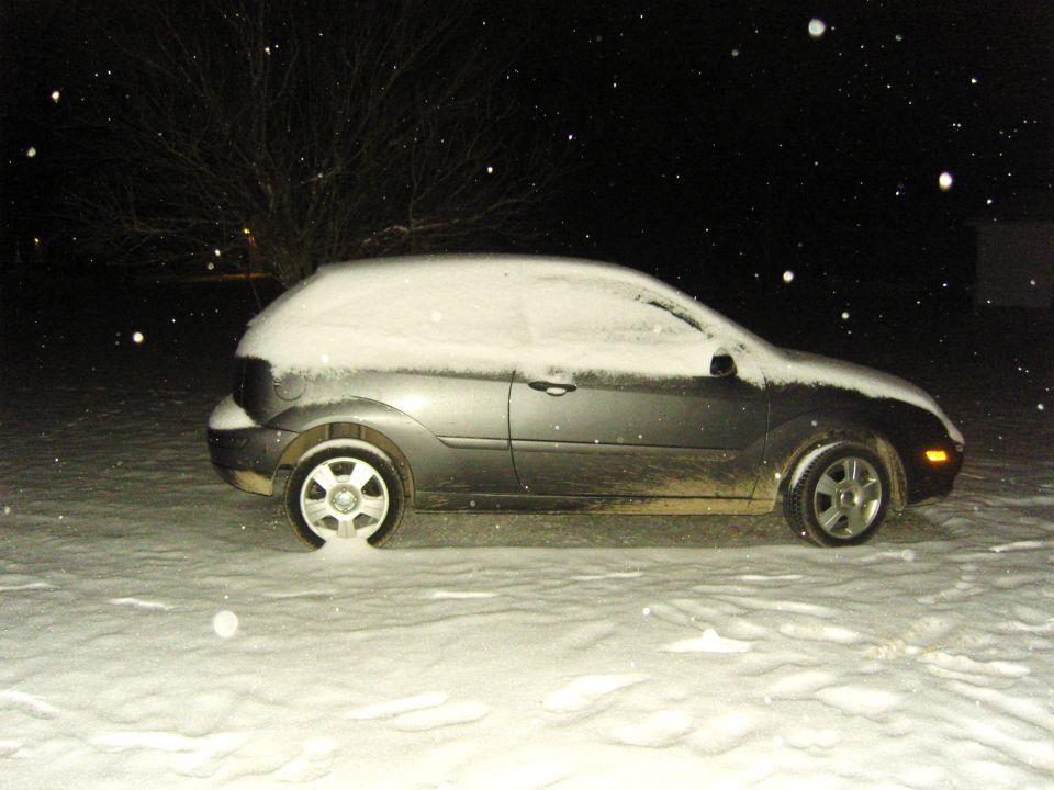 gray hatchback covered in snow, parked outside at night