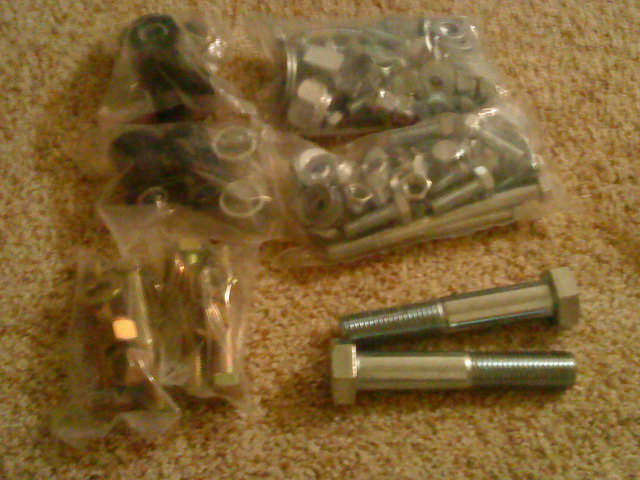 Several plastic bags filled with nuts, bolts, and other hardware, with two large bolts in the foreground