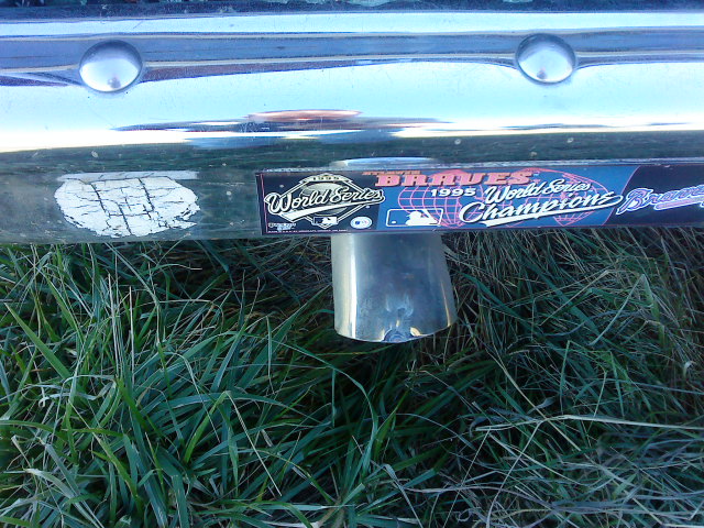 Chrome exhaust pipe protruding from a scratched bumper with a 'Braves 1995 World Series Champions' sticker