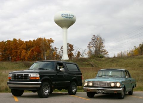 1995 Ford Bronco - A 1995 Ford Bronco and an older sedan are parked in front of a water tower with autumn foliage in the background.