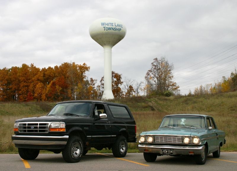 Black 1995 Ford Bronco and a light blue 1960s sedan parked near a White Lake Township water tower