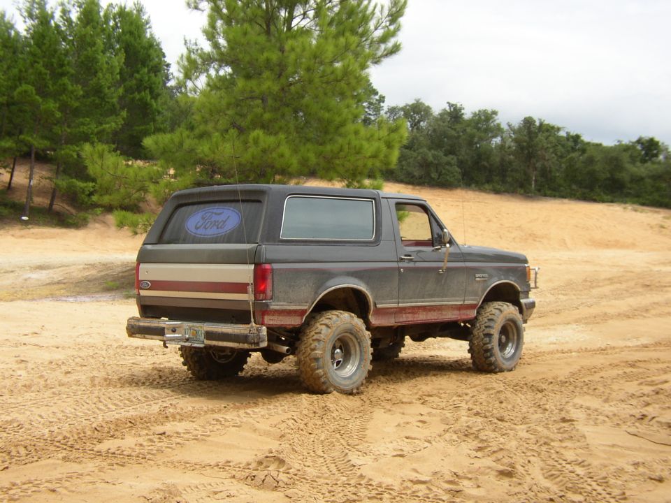 Gray and tan two-tone full-size Ford Bronco with mud tires parked on sand at an off-road park