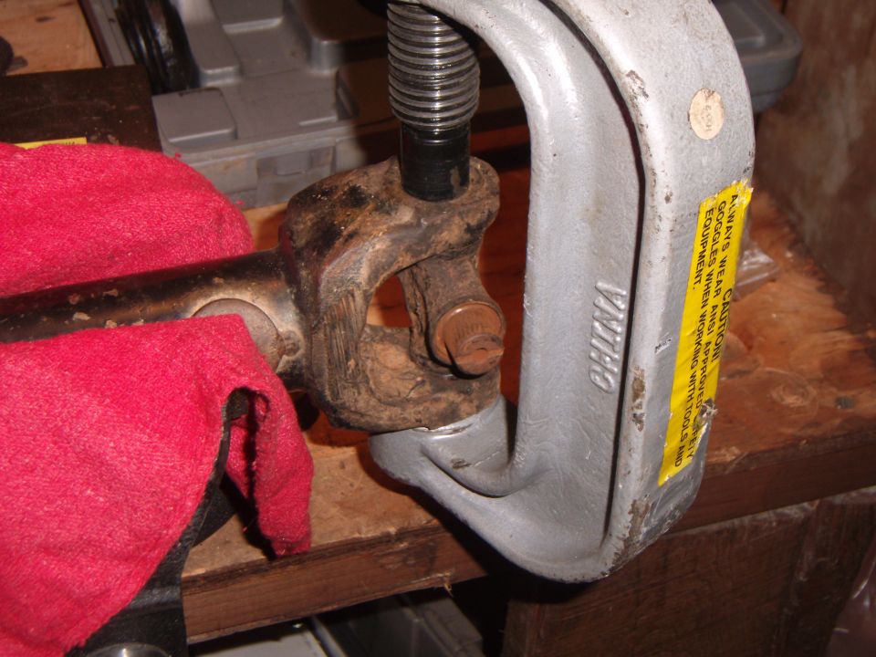 Universal joint held in a vise with a red cloth nearby. A yellow caution sticker is on the vise