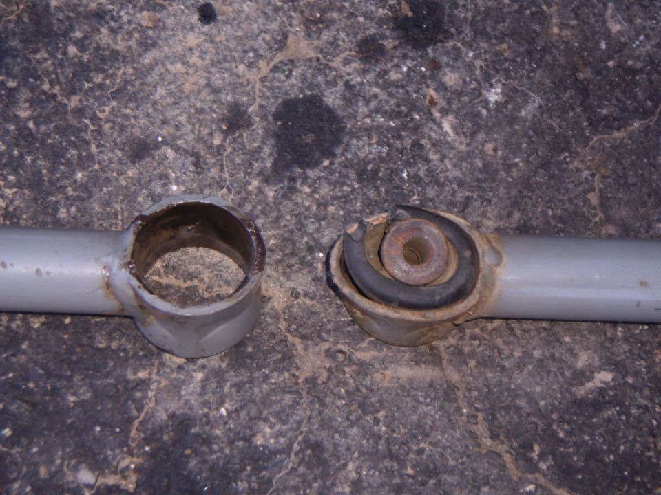 Worn suspension bushing and metal housing on a gray metal rod against a concrete surface