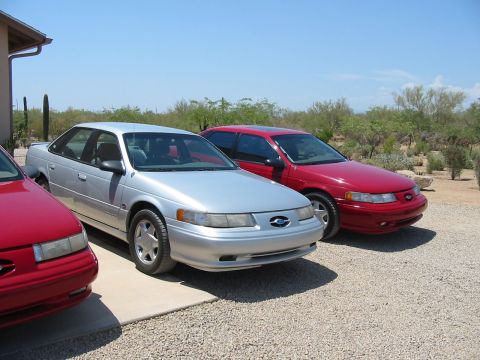 1993 Ford Taurus - Two Ford Taurus sedans, one silver and one red, are parked outside on a sunny day.